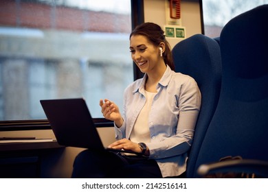 Young happy woman using laptop and talking to someone via video call while traveling by train. 