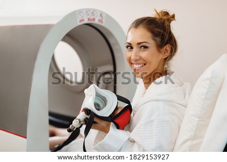 Young happy woman using oxygen mask during hyperbaric oxygen therapy at health spa. 