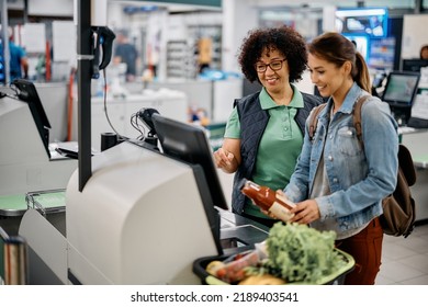 Young happy woman using self-service checkout with help of supermarket worker. 
