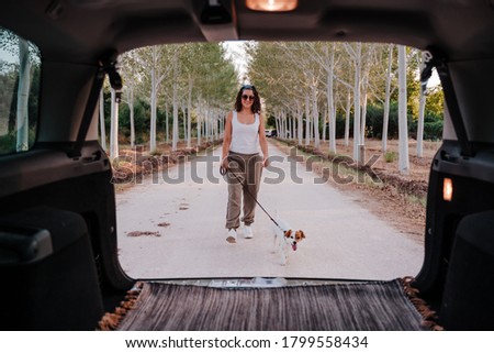 young happy woman walking outdoors with her dog. Travel concept. View from inside the car