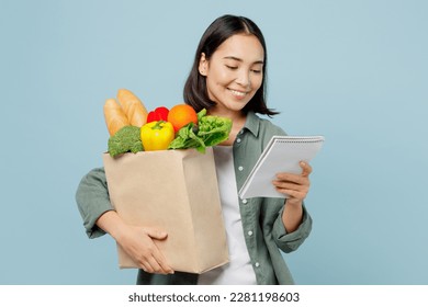 Young happy woman wear casual clothes hold brown paper bag with food products read liat of ingredients isolated on plain blue cyan background studio portrait. Delivery service from shop or restaurant - Shutterstock ID 2281198603