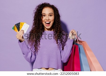 Young happy woman wear pullover hold paper package bags after shopping many mock up of credit bank card isolated on plain pastel light purple color background studio. Black Friday sale buy day concept