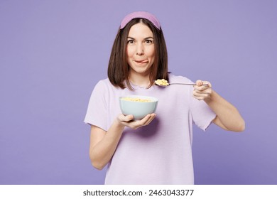 Young happy woman wear pyjamas jam sleep eye mask rest relax at home eat breakfast muesli cereals with milk fruit in bowl isolated on plain pastel light purple background. Good mood night nap concept - Powered by Shutterstock