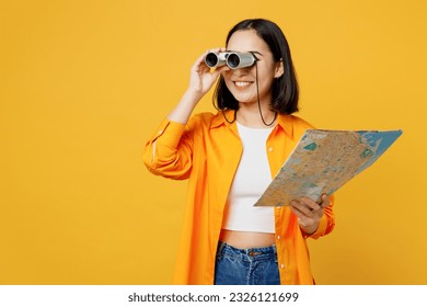 Young happy woman wear summer casual clothes hold in hand map use binoculars isolated on plain yellow background. Tourist travel abroad in free spare time rest getaway Air flight trip journey concept