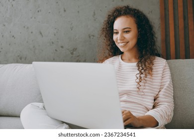 Young happy IT woman wearing casual clothes sits on grey sofa couch hold use work on laptop pc computer stay at home hotel flat rest relax spend free spare time in living room indoor. Lounge concept - Shutterstock ID 2367234541