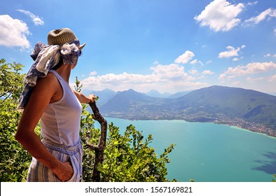 A young happy woman wearing a hat admires a panoramic view on the Lake Annecy from mont Veyrier to mont Baron hiking track, France