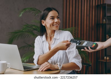 Young happy woman in white shirt hold pay waiter hold wireless bank payment terminal process acquire credit card sit at table in coffee shop cafe restaurant indoor work or study on laptop pc computer - Shutterstock ID 2217236257