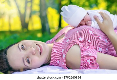young happy woman who gave birth to a baby is lying on her back with the baby lying on her stomach in a park on a warm sunny day