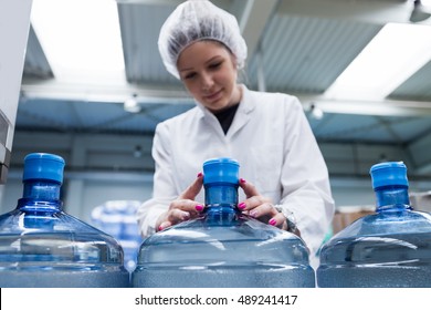 Young happy woman worker in factory checking water bottles or gallons before shipment. Inspection quality control. People at work.
