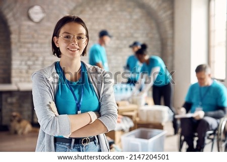 Young happy woman working as volunteer and standing with her arms crossed at donation center. 