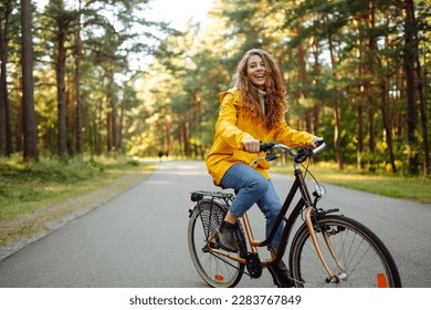 Young happy woman in a yellow coat rides a bicycle in a sunny park. Beautiful woman enjoys autumn nature. Relax, nature concept. Lifestyle. - Powered by Shutterstock