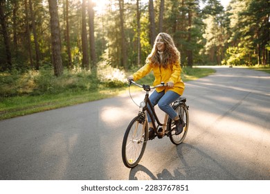 Young happy woman in a yellow coat rides a bicycle in a sunny park. Beautiful woman enjoys autumn nature. Relax, nature concept. Lifestyle. - Powered by Shutterstock