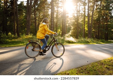 Young happy woman in a yellow coat rides a bicycle in a sunny park. Beautiful woman enjoys autumn nature. Relax, nature concept. Lifestyle.