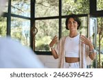 Young happy woman yoga coach training group class yoga meditation session sitting in yoga pose in studio speaking to community teaching people during retreat holistic mind body health therapy.