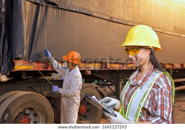 young harbor worker talking on the\
walkie-talkie at truck,Young woman in safety hat holding\
waklie-talkie front of truck\
background.