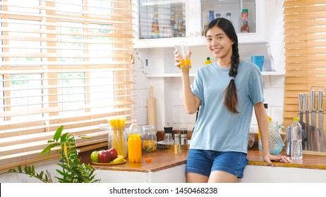 Young Healthy Asian Woman Drinking Orange  Juice, Happy Asia Teenager Girl Holding Glass Of Orange Juice While Standing In Kitchen At Home, Food And Drink Healthy Lifestyle