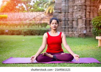 Young healthy beautiful girl in sportive red top and leggings practicing yoga at park sitting in lotus pose on yoga mat meditating relaxed with closed eyes, Mindfulness meditation concept - Powered by Shutterstock