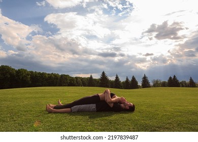 Young Healthy Couple Doing Yoga In The Sunny Summer Park. Fitness And Healthy Lifestyle