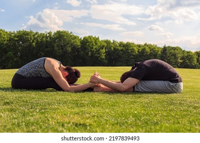 Young Healthy Couple Doing Yoga In The Sunny Summer Park. Fitness And Healthy Lifestyle