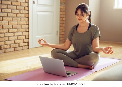 Young Healthy Indian Woman Wear Sportswear Meditating Watching Live Online Tv Pilates Class Tutorial On Laptop Computer At Home Doing Yoga Virtual Training Fitness Workout Sport Exercise In Apartment.