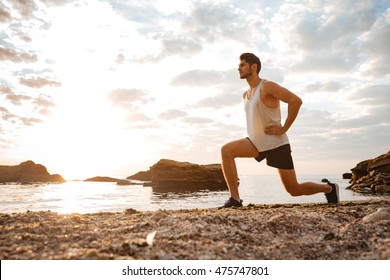 Young Healthy Man Athlete Doing Squats At The Beach At Sunset