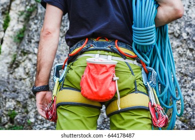 Young healthy man wearing in climbing equipment with rope standing in front of a stone rock and preparing to climb - Powered by Shutterstock