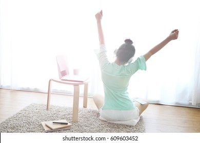 Young healthy woman back view at modern home sitting on floor with computer and coffee cup in front of window relaxing in her living room working on internet, Wake up. - Powered by Shutterstock