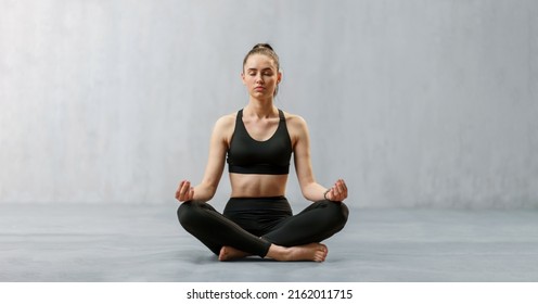 Young healthy woman in black sportsclothes practising yoga in studio, in a yoga position, copy space
