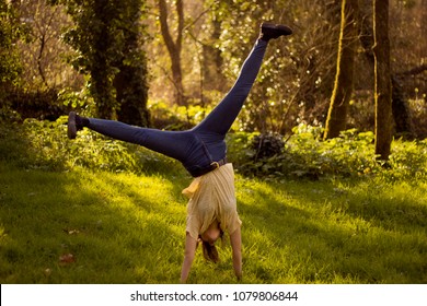 A Young Healthy Woman Giving A Cartwheel  In The Air In A Lovely Forest. A Young Model Posing Happy During A Summer Afternoon