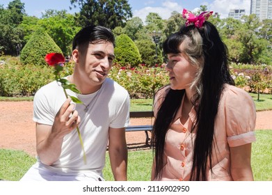 Young Heterosexual Caucasian Hispanic Latin Couple On A Date In The Park Talking, Man With A Flower In His Hand Talks To His Girlfriend, Valentines Day Concept.