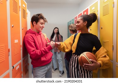 Young high school students meeting and greeting near locker in campus hallway talking and high fiving. - Shutterstock ID 2190204331