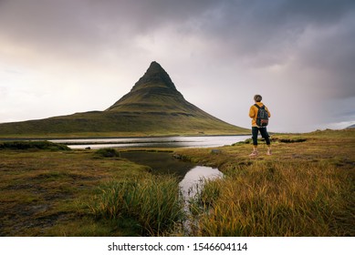Young hiker with a backpack looks at the Kirkjufell mountain in Iceland. This 463 m high mountain is located on the north coast of Iceland's Snaefellsnes peninsula.
