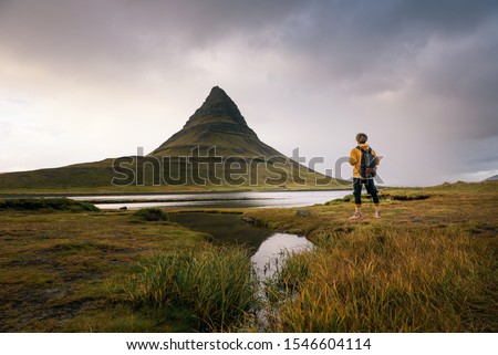 Young hiker with a backpack looks at the Kirkjufell mountain in Iceland. This 463 m high mountain is located on the north coast of Iceland's Snaefellsnes peninsula.