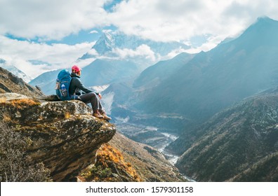 Young hiker backpacker female sitting on the cliff edge and enjoying Ama Dablam 6,812m peak view during Everest Base Camp (EBC) trekking route near Phortse, Nepal. Active vacations concept image - Powered by Shutterstock