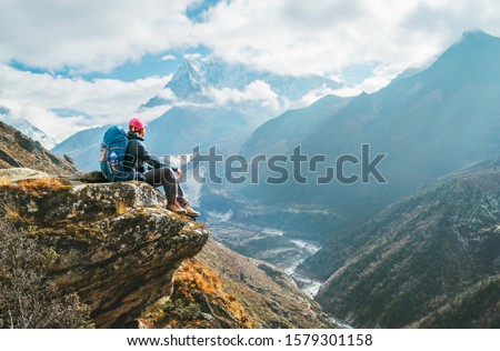 Young hiker backpacker female sitting on the cliff edge and enjoying Ama Dablam 6,812m peak view during Everest Base Camp (EBC) trekking route near Phortse, Nepal. Active vacations concept image