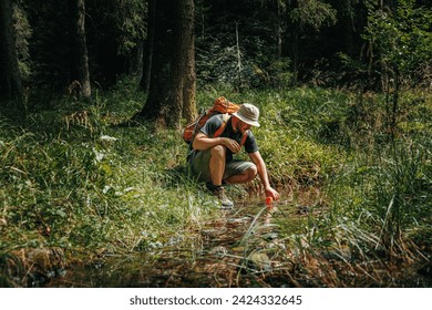 Young Hiker Man Relishes the Outdoors, Filling His Bottle from a Woodland Stream on the Expedition - Powered by Shutterstock