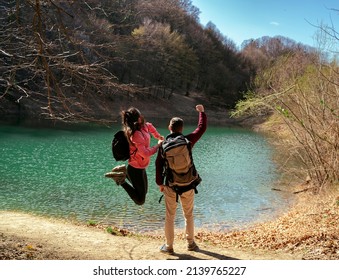 Young hikers celebrating success, they reached their destination, enjoying beautiful scenery, woman jumping ,man holding fist in the air 