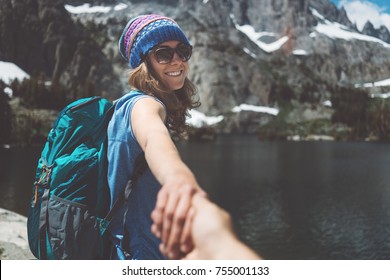 Young hiking couple with backpacks traveling, woman guiding by the hand into mountain wilderness