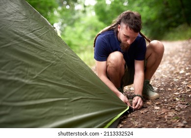 Young Hippie Hiker Setting Up His Tent In The Forest, Pitching In A Forest Clearing, Getting Ready For A Camping Sleepover