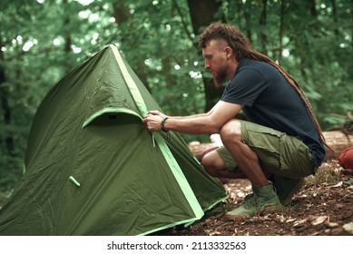 Young Hippie Hiker Setting Up His Tent In The Forest, Pitching In A Forest Clearing, Getting Ready For A Camping Sleepover