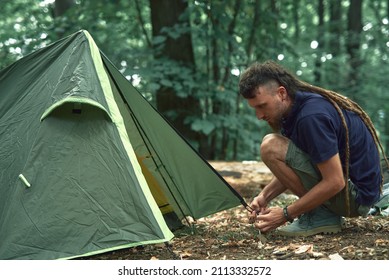 Young Hippie Hiker Setting Up His Tent In The Forest, Pitching In A Forest Clearing, Getting Ready For A Camping Sleepover