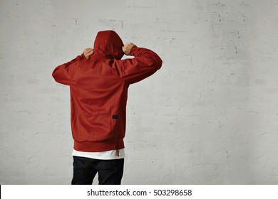 A young hipster adjusts the hood of his brownish red parka, back view, shot in studio with white walls - Powered by Shutterstock