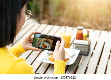 Young Hipster Asian Blogger Take Photo Of Food, Plate, Healthy Recipe, Lunch Meal, Breakfast Share To Story In Social Media At Restaurant Or Home. Screen Showing On Moblie Phone With Blogger Concept.