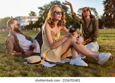 Young Hipster Company Of Friends Having Fun Together In Park Smiling Listening To Music On Small Wireless Speaker, Summer Style Season, Drinking Coffee