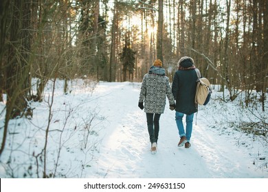 Young Hipster Couple Having A Walk In Winter Forest With Bag Alone