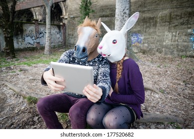 Young Hipster Couple Horse And Rabbit Mask Using Tablet At The Park