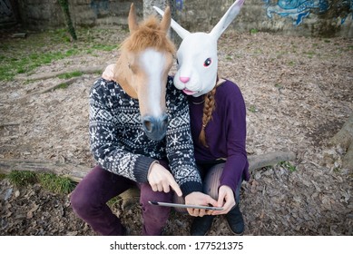 Young Hipster Couple Horse And Rabbit Mask Using Tablet At The Park