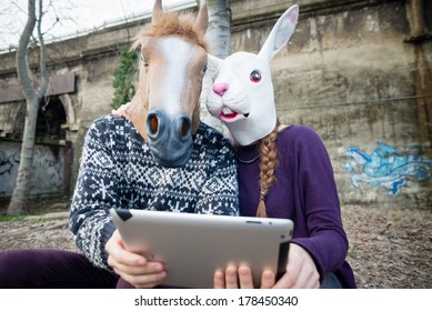 Young Hipster Couple Horse And Rabbit Mask Using Tablet At The Park