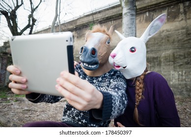 Young Hipster Couple Horse And Rabbit Mask Using Tablet At The Park