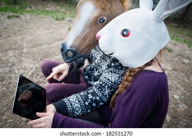 Young Hipster Couple Horse And Rabbit Mask Using Tablet At The Park